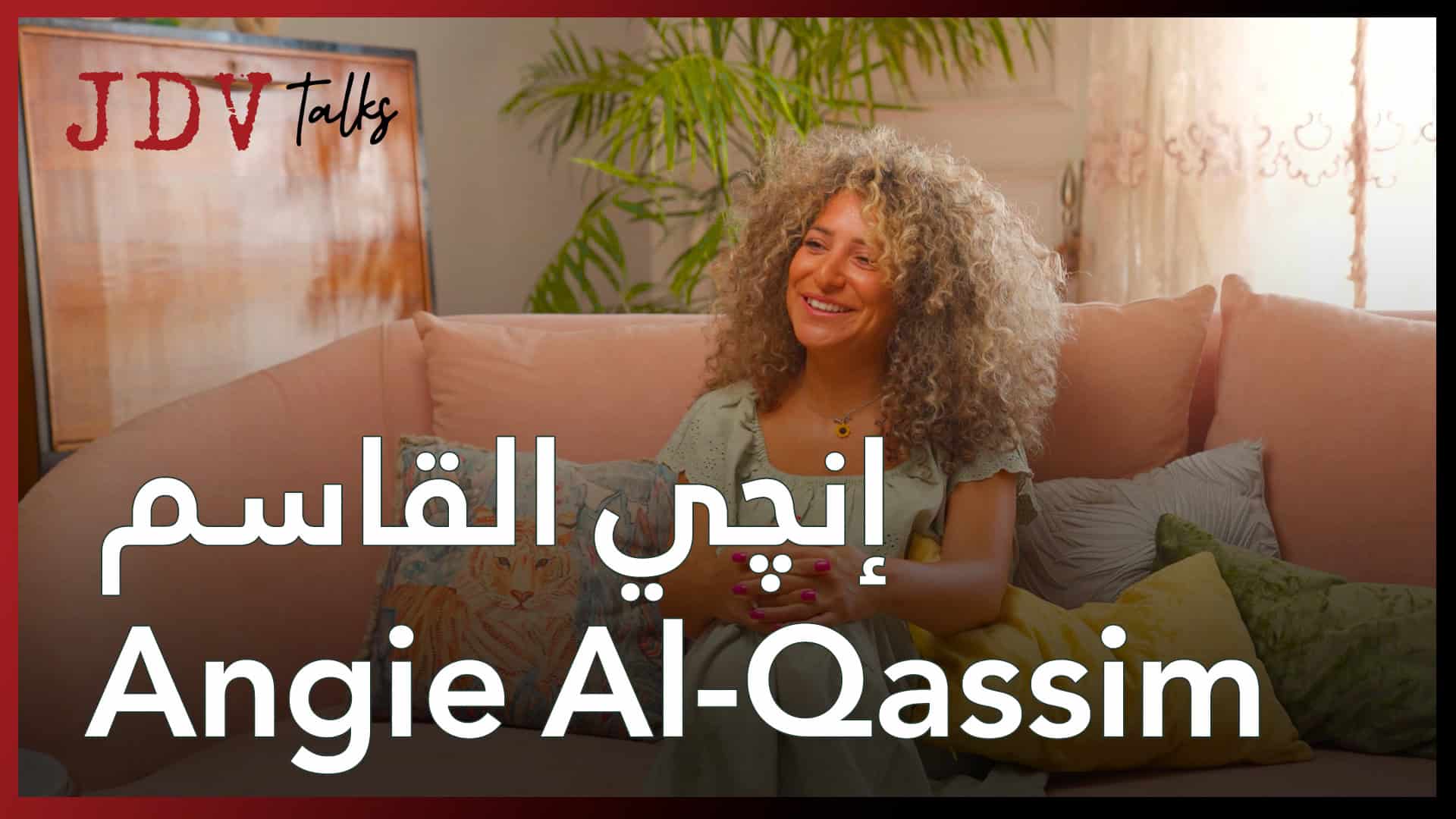 Angie Al-Qassim smiling while sitting on a sofa in a cozy living room with plants and sunlight.