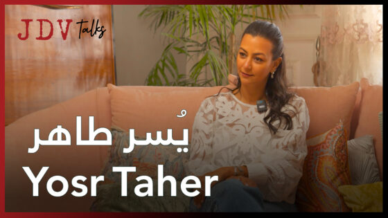 Yosr Taher sitting on a sofa during an interview, smiling and engaging in conversation.