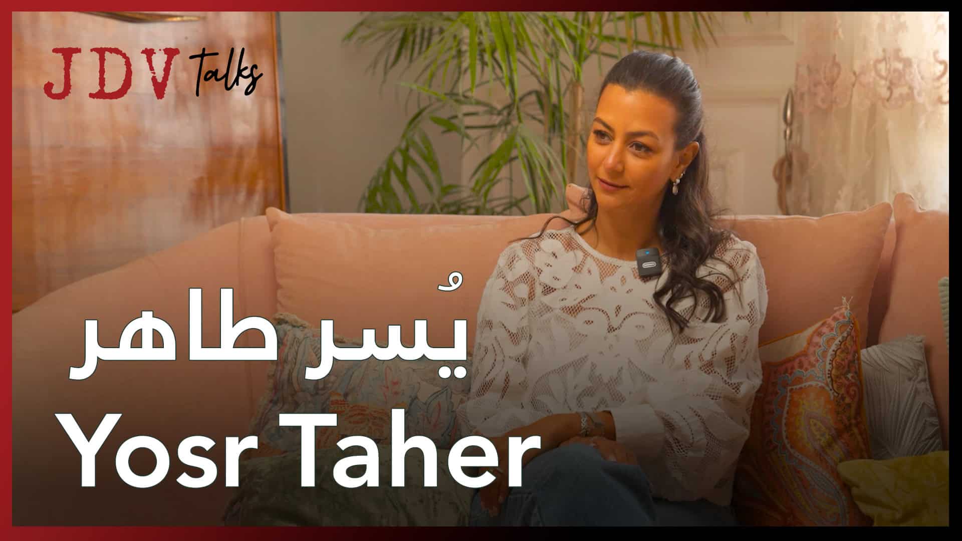 Yosr Taher sitting on a sofa during an interview, smiling and engaging in conversation.