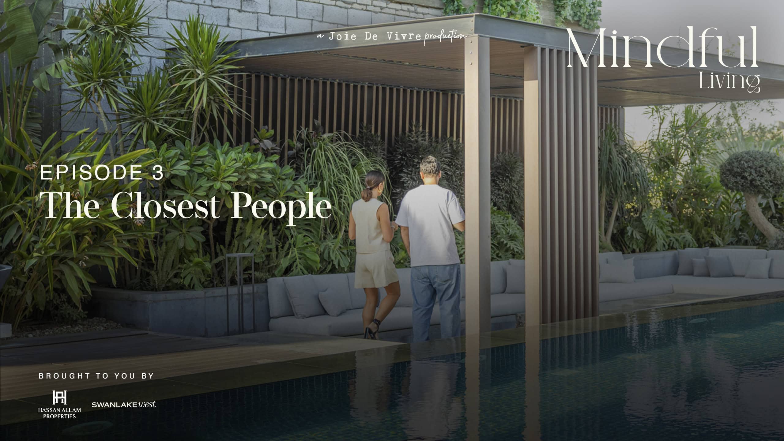 Two people walking by a modern outdoor pool area with lush greenery and wooden structures, promoting mindful living and close relationships.