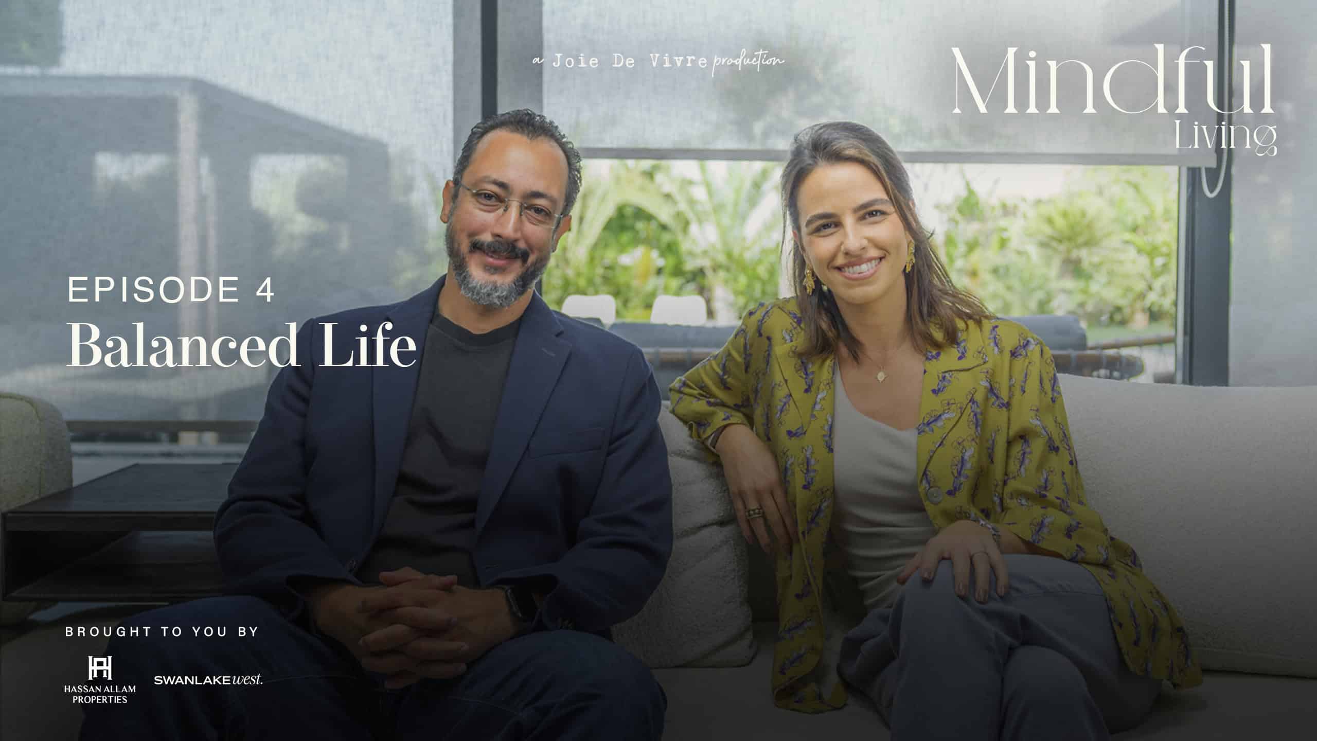 Two individuals, a man and a woman, sitting on a sofa in a modern, well-lit living room, smiling at the camera, representing balanced living and mindfulness.