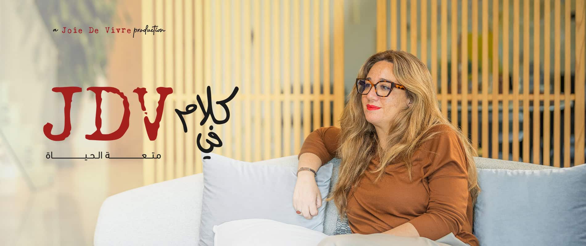 Insightful woman with glasses and red lipstick sitting on a cozy sofa in a modern, warm interior space, reflecting confidence and professionalism for personal growth or lifestyle branding.