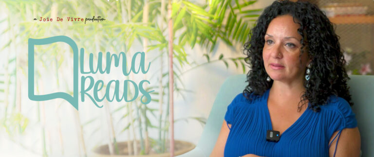 Reading enthusiast woman in blue dress with curly hair, sitting in cozy environment, promoting literacy and love for reading, with "Luma Reads" logo in the background.