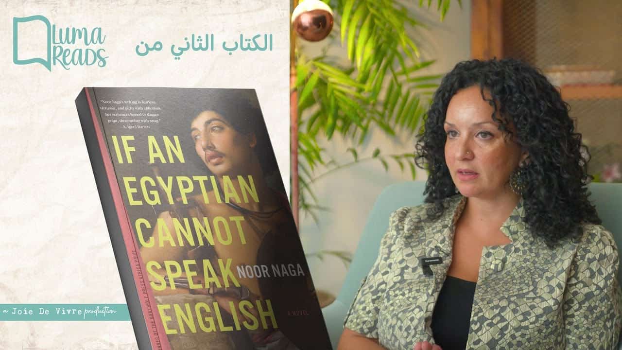 A woman with curly black hair sitting indoors next to a potted plant, discussing or presenting a book titled "If an Egyptian Cannot Speak English" by Noor Naga. The setting appears cozy and professional, ideal for literary or cultural discussions.